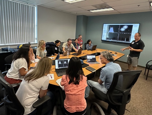 Small-group lecture session with students around a conference table reviewing cytometry data